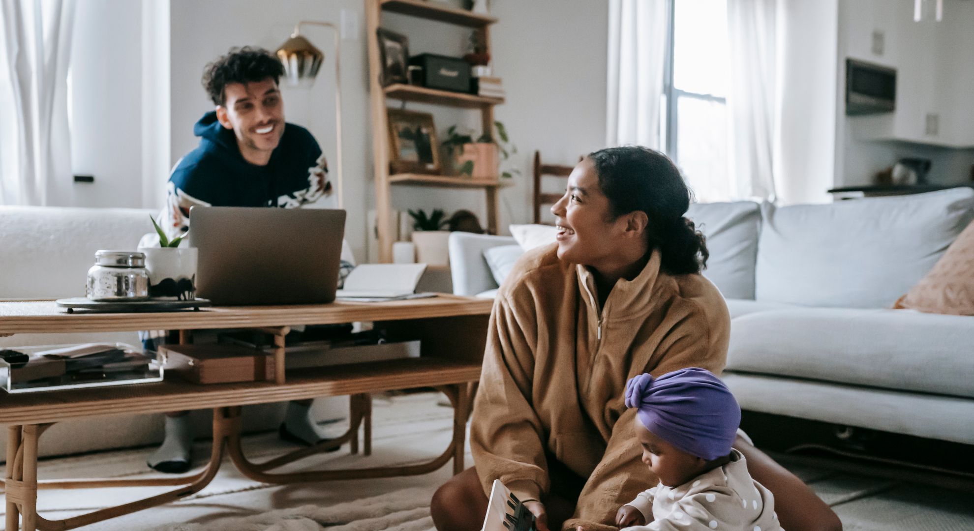 woman sits with child on floor and smiles at man on couch