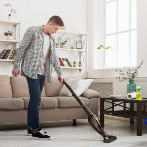 a new york city resident vacuuming the carpet cleaning his apartment