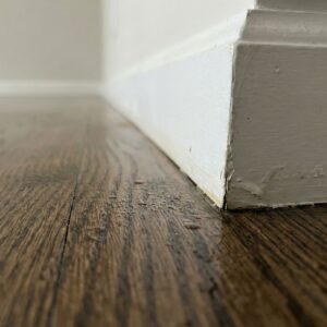 A close-up view of wet hardwood flooring and a swollen baseboard showing signs of moisture saturation.